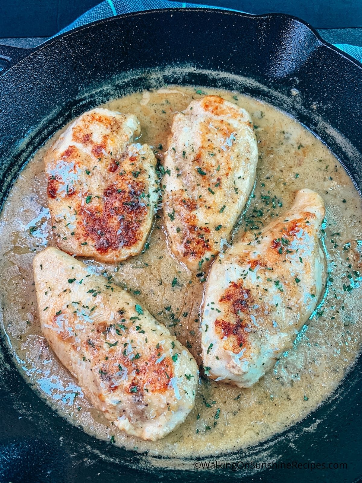 Browned chicken cutlets in garlic butter sauce in cast iron skillet.