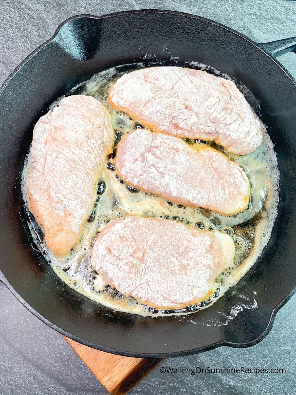 Chicken cutlets cooking in cast iron skillet pan.