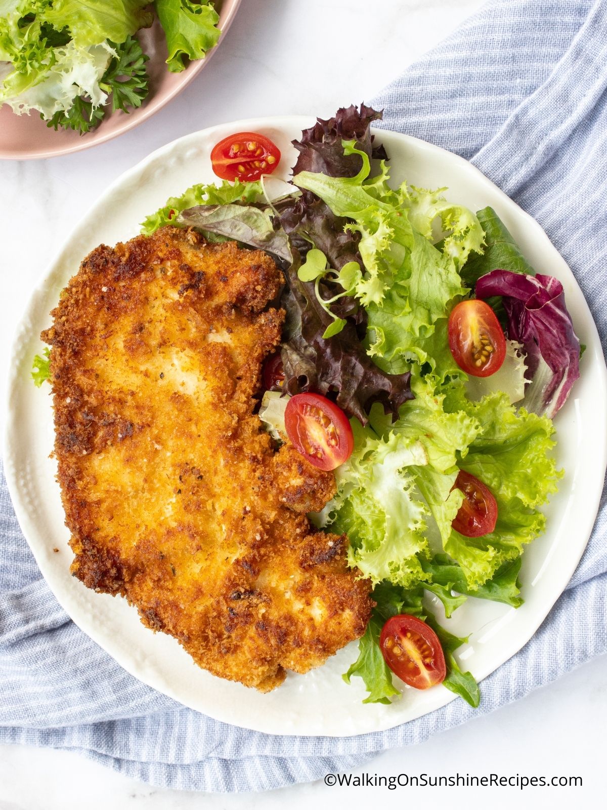 chicken cutlets with Italian breadcrumbs on white plate with salad and dressing in small bowl.