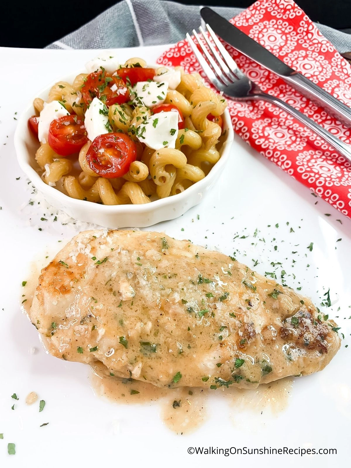 Sauteed chicken cutlets on white plate with pasta and tomatoes in bowl.