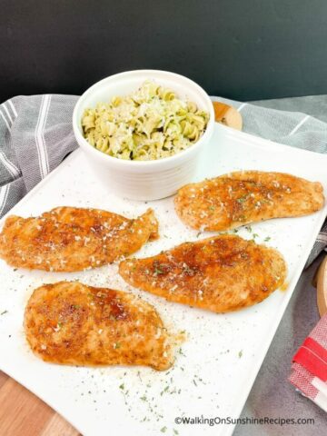 Baked Moist Chicken Cutlets on white platter with pasta in small bowl.