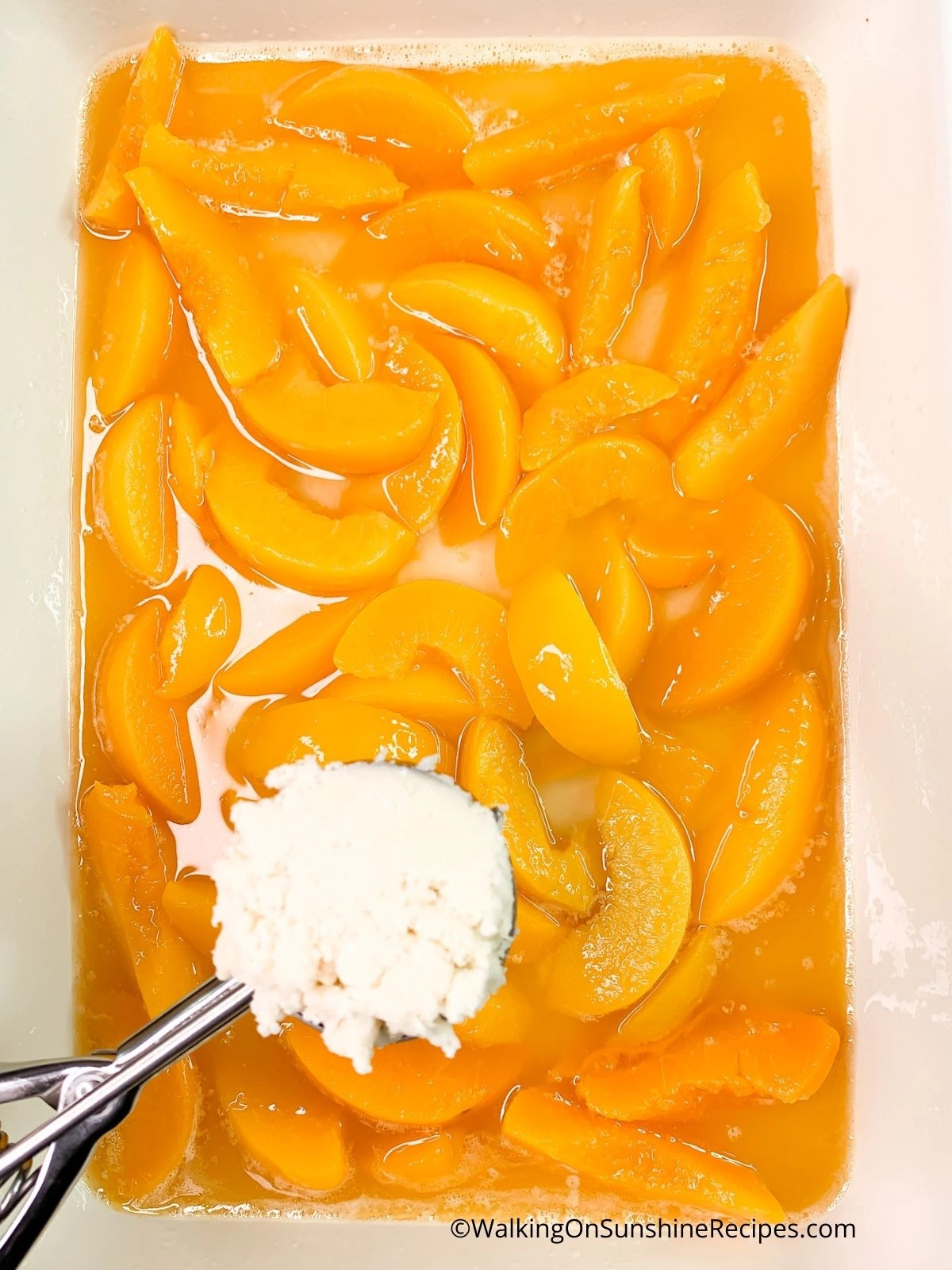 Use a cookie scoop to add white cake mix cobbler topping to canned peaches.