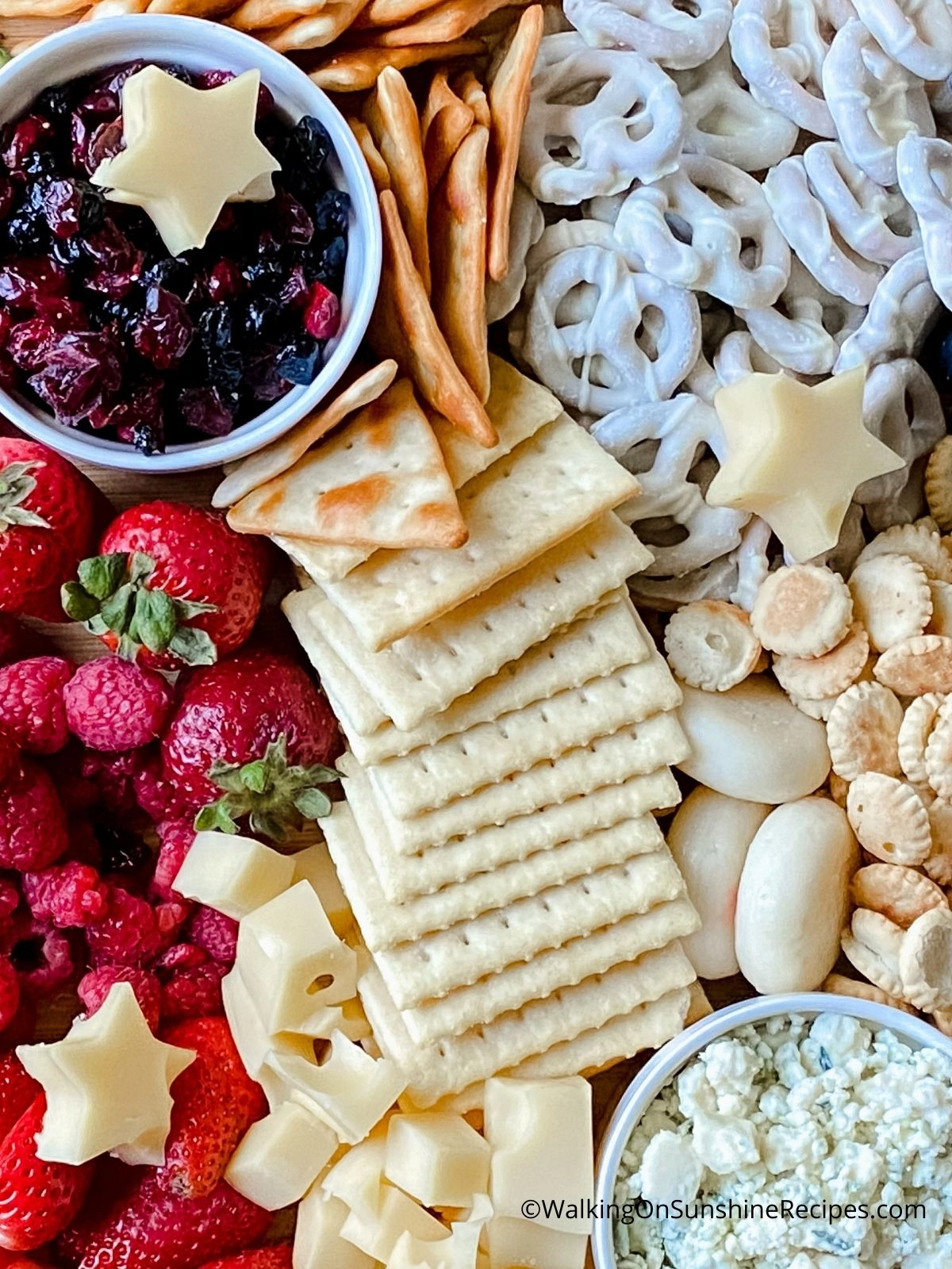 fruit, chocolate covered pretzels, crackers and cheeses on a board. 