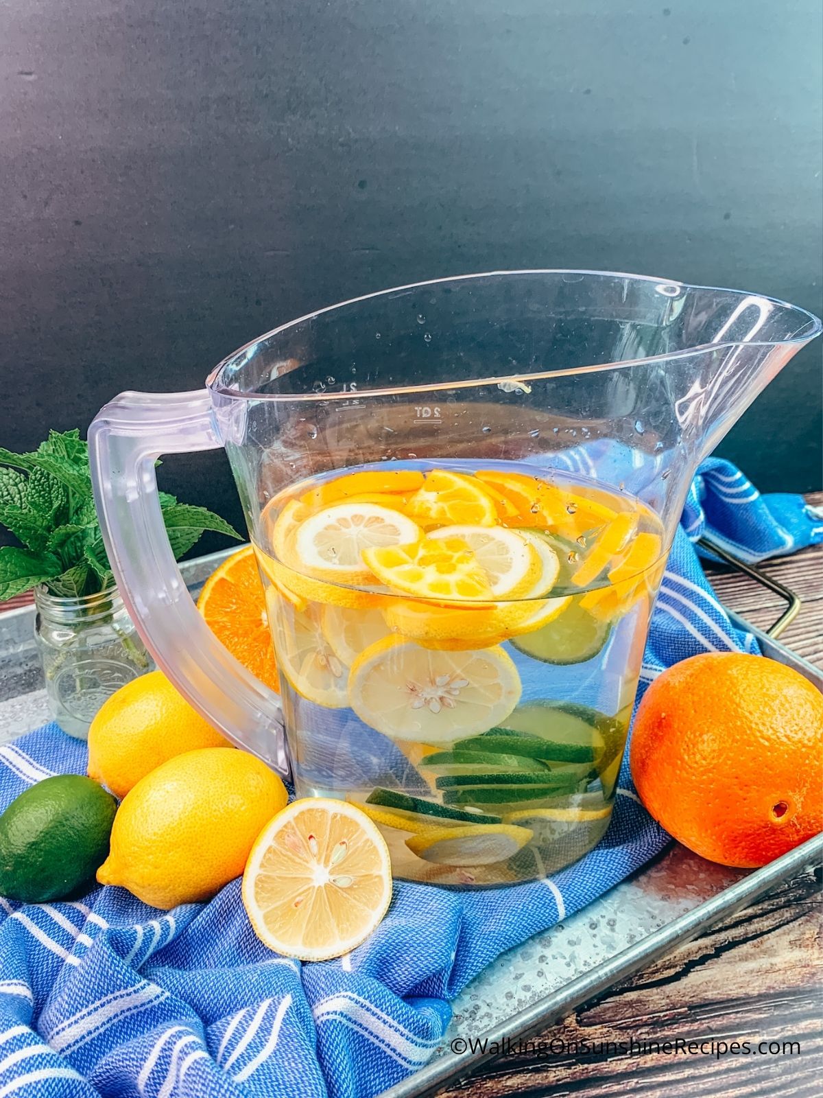 sliced lemons, limes and oranges in a pitcher of water on galvanized tray. 