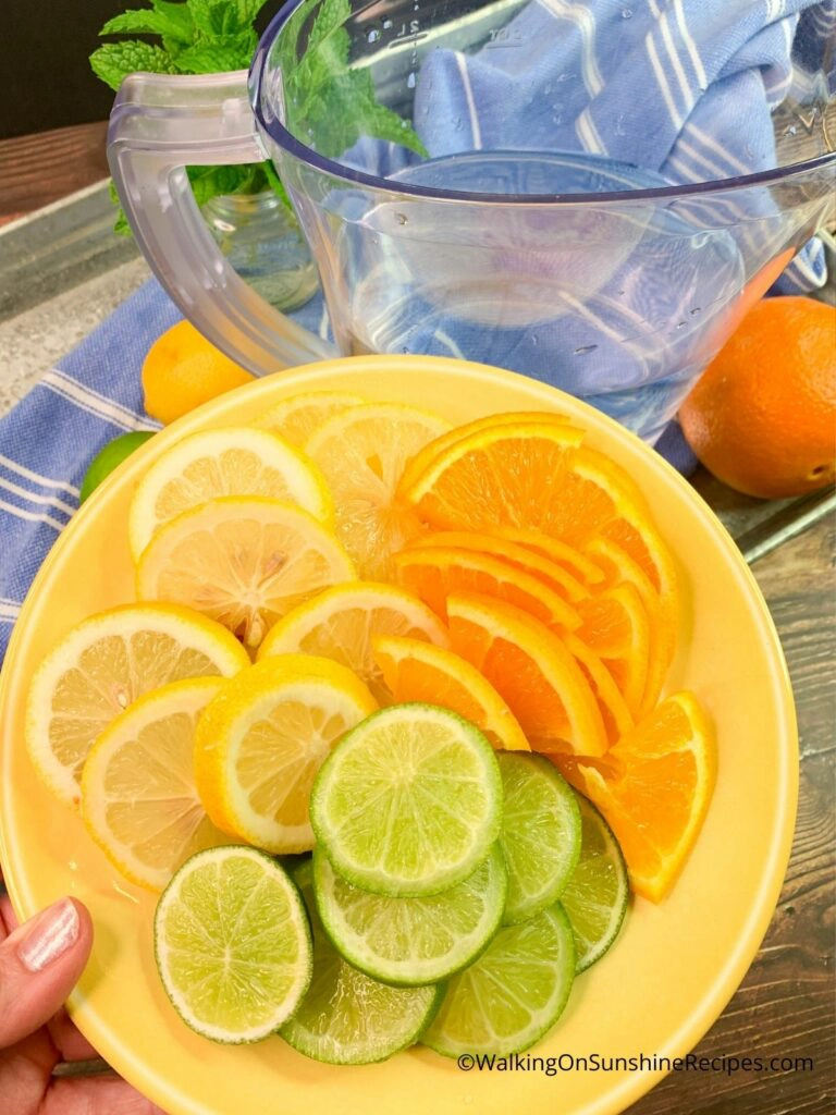Adding sliced limes, lemons and oranges to water. 