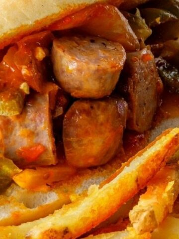 Sausage and peppers sandwich in a hoagie roll topped with sautéed bell peppers and onions.