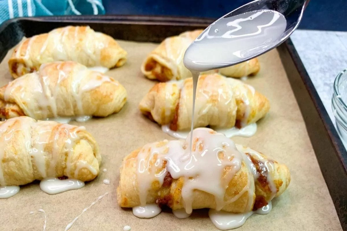 Pumpkin Pie Crescent Rolls with a spoonful of glaze being poured onto the crescent.