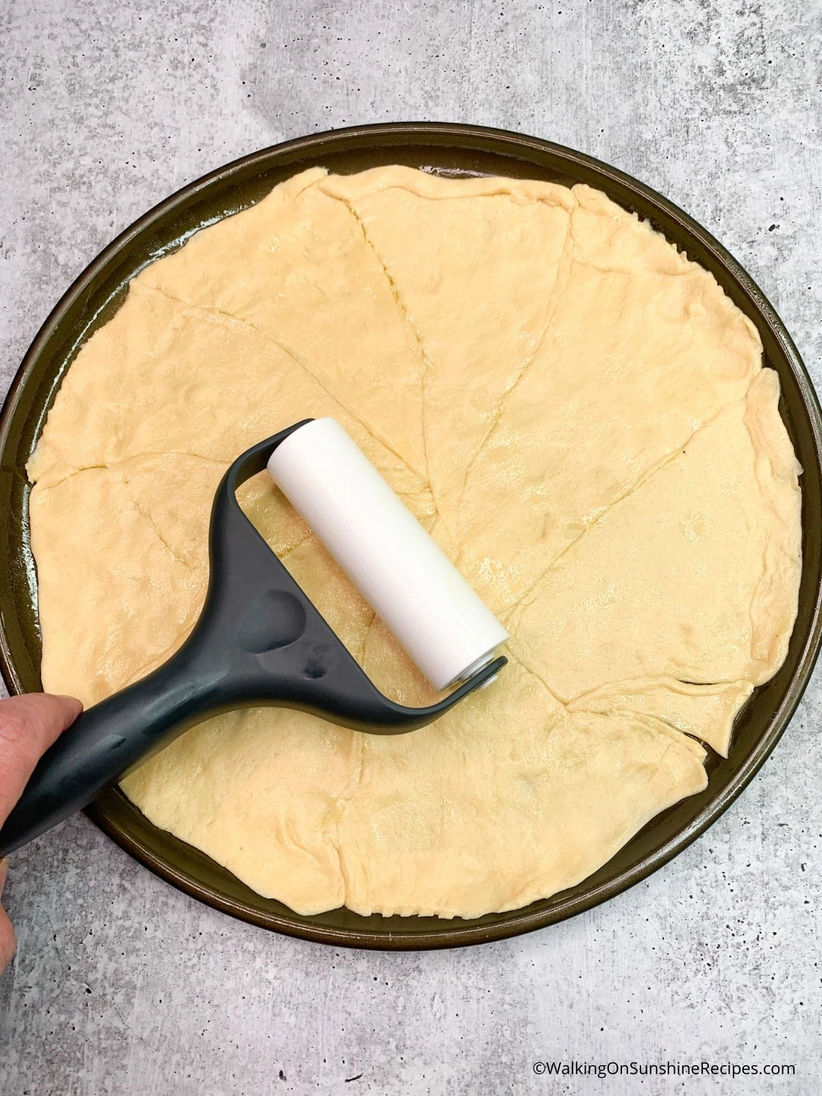 Rolling out crescent roll dough in pizza pan.