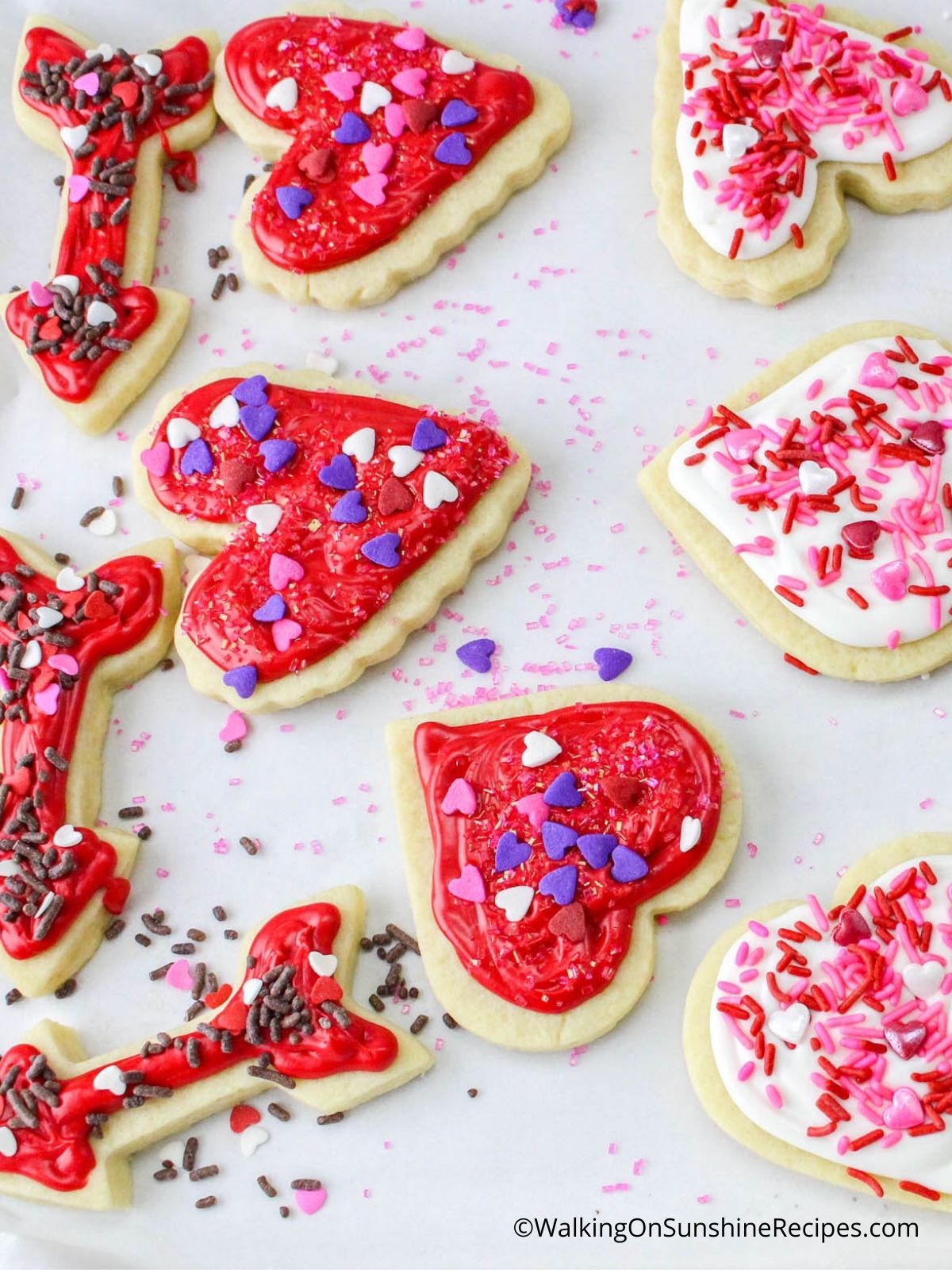 Heart shaped sugar cookies decorated with red frosting and sprinkles. 