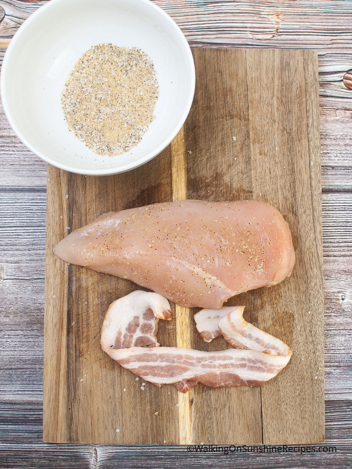 raw chicken on cutting board with piece of bacon.