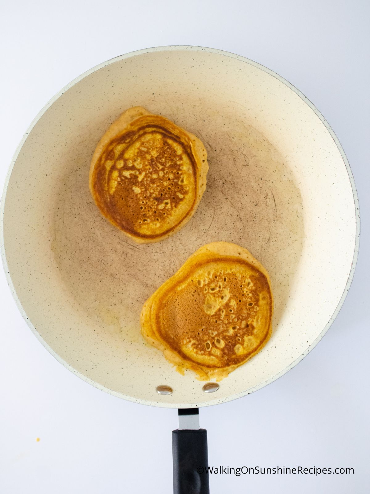 two pumpkin pancakes browning in a pan
