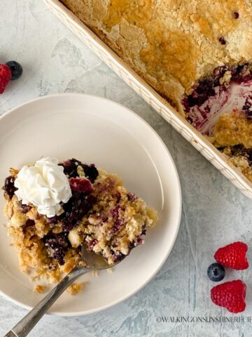 Berry Dump Cake on plate with fresh whipped cream.