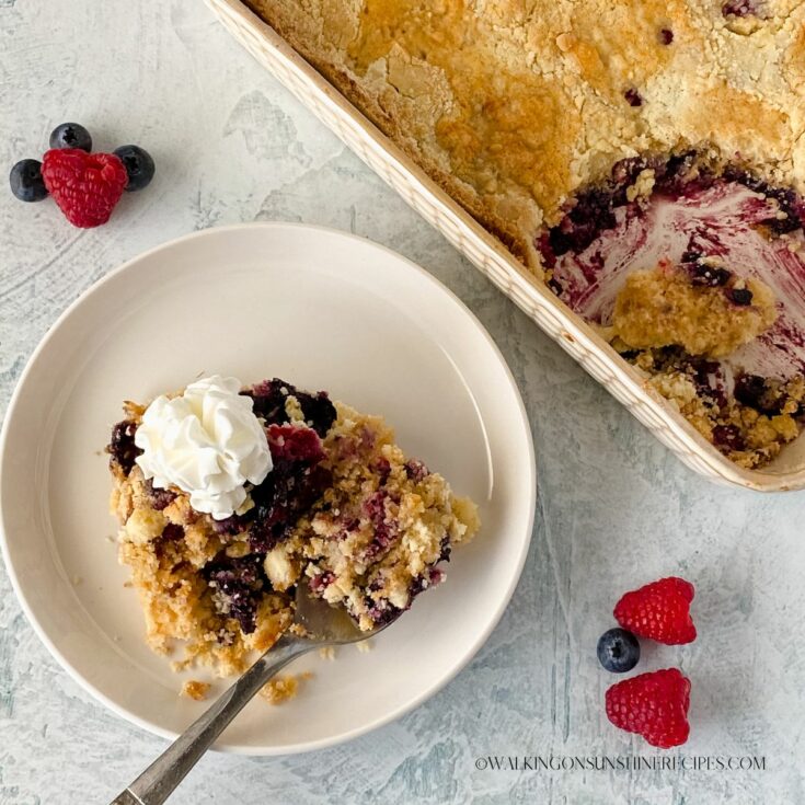 Berry Dump Cake on plate with fresh whipped cream.