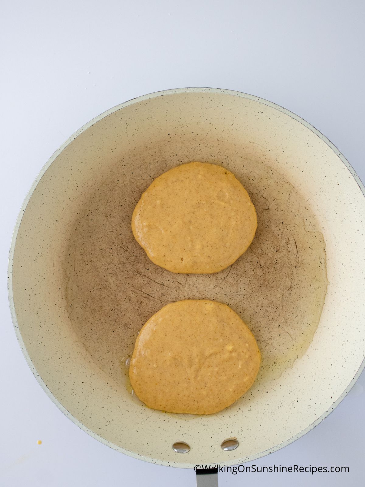 two pumpkin pancakes cooking in a pan