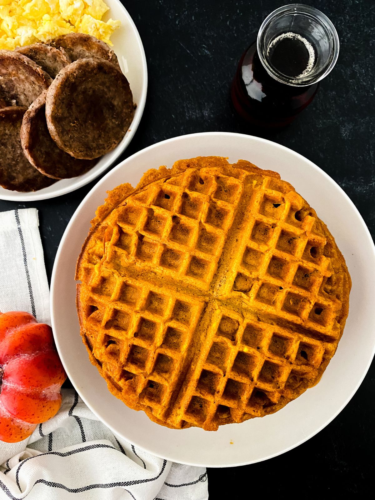 Homemade Pumpkin Waffles on Plate. Plate of sausage and eggs to the left.