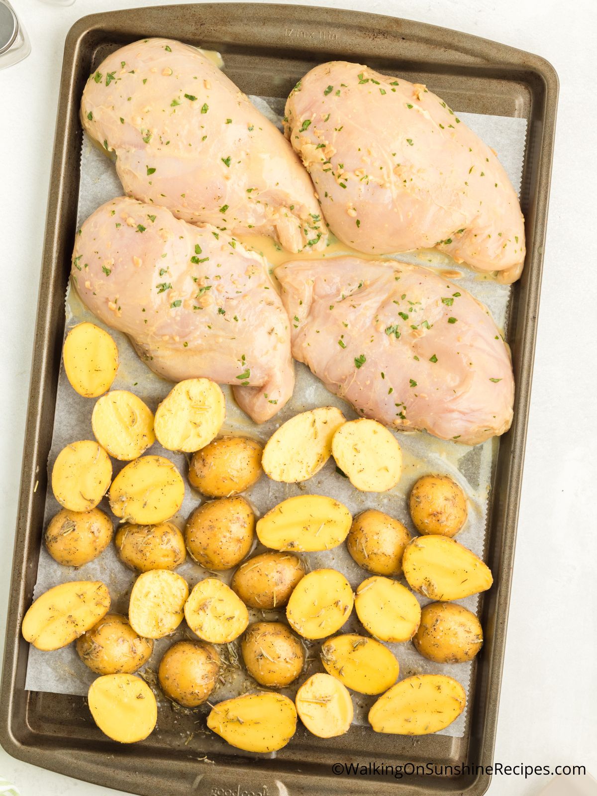 raw chicken cutlets on baking pan with Yukon gold potatoes.