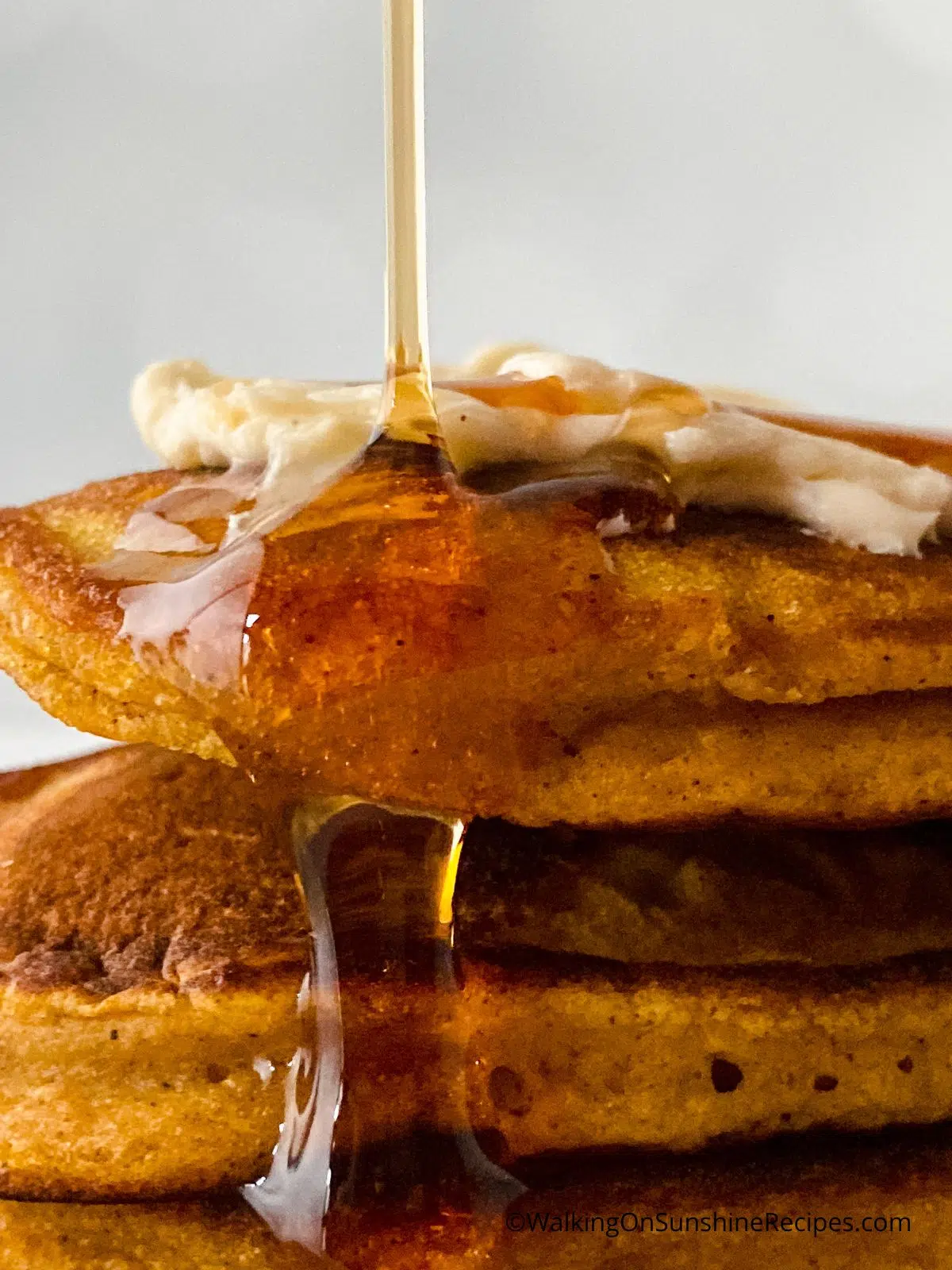 syrup being poured onto a stack of pumpkin pancakes