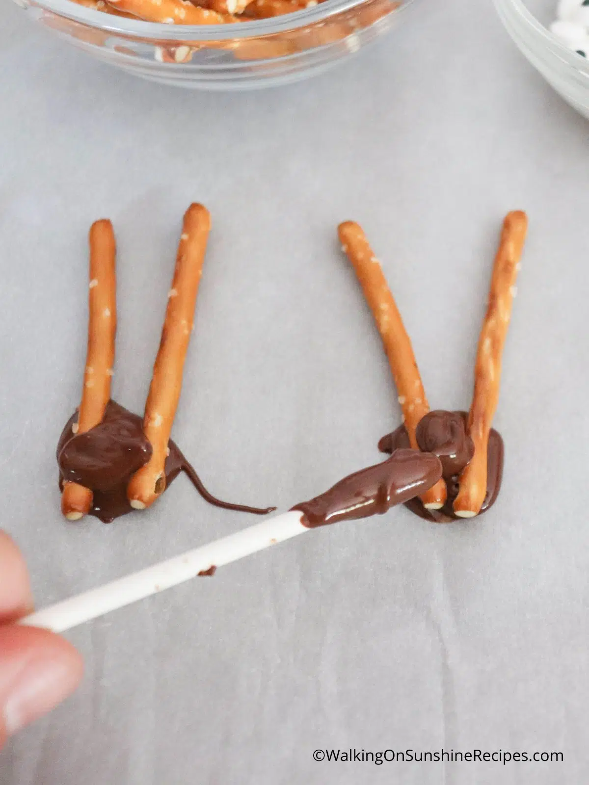 add melted chocolate to the back of pretzel sticks.
