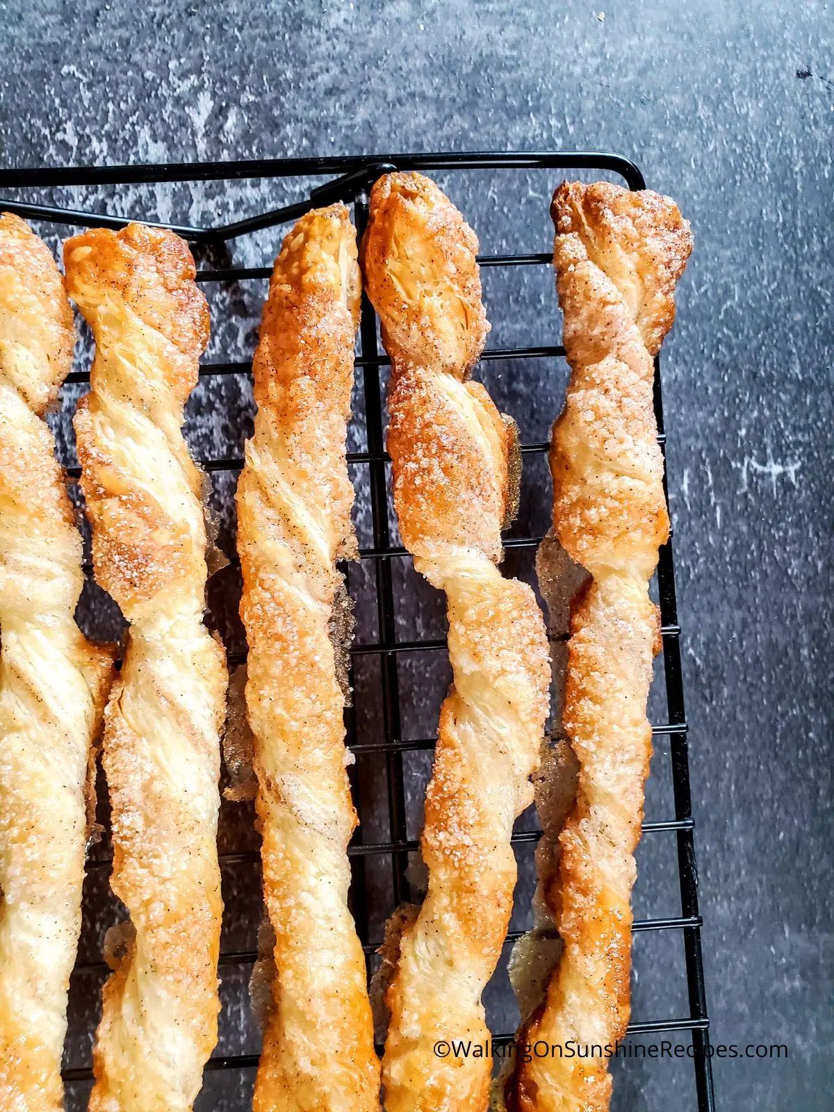 Baked puff pastry cinnamon twists cooling on baking rack.