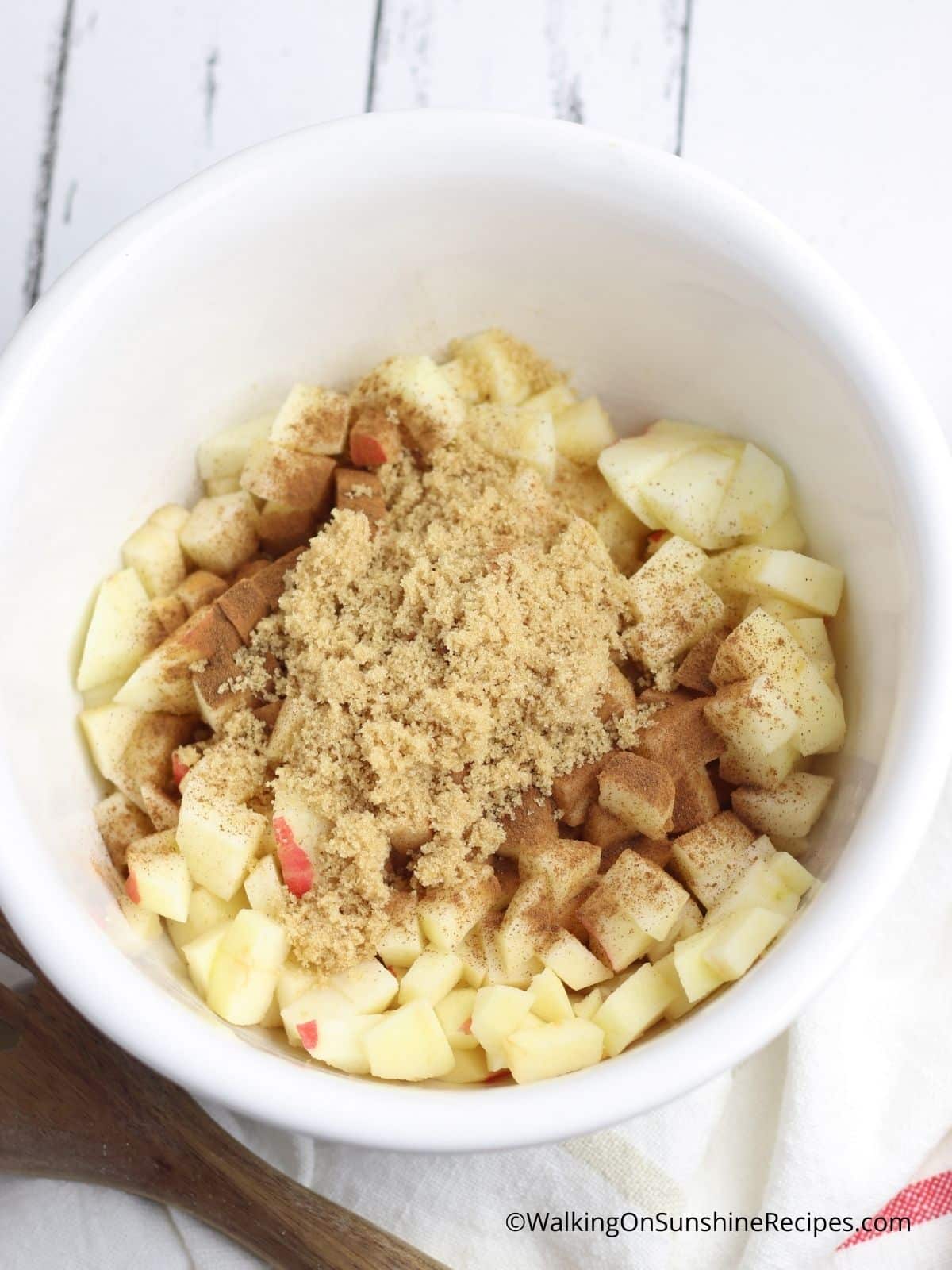 brown sugar on top of chopped apples in white bowl.