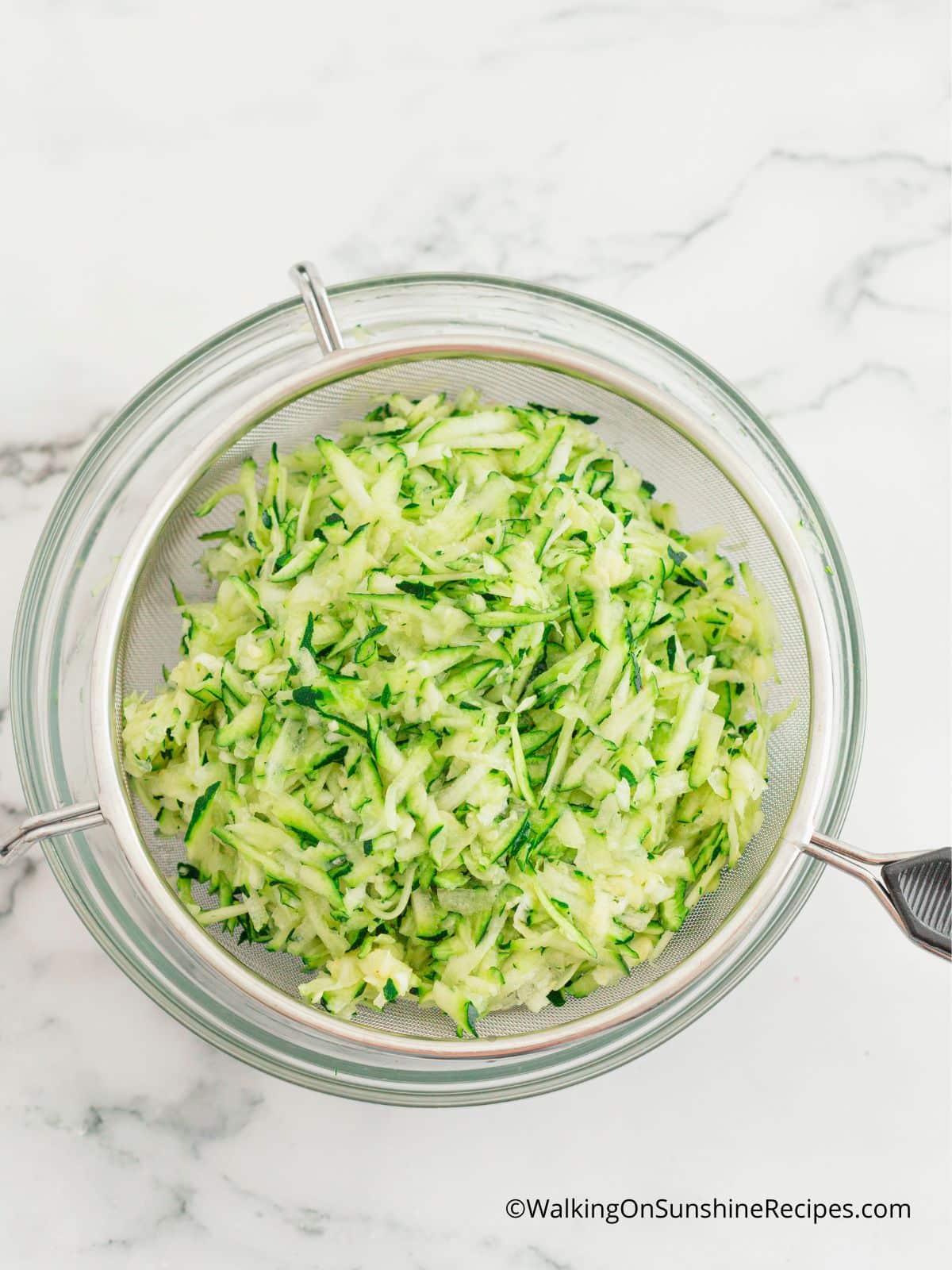grated zucchini in sieve over glass bowl.