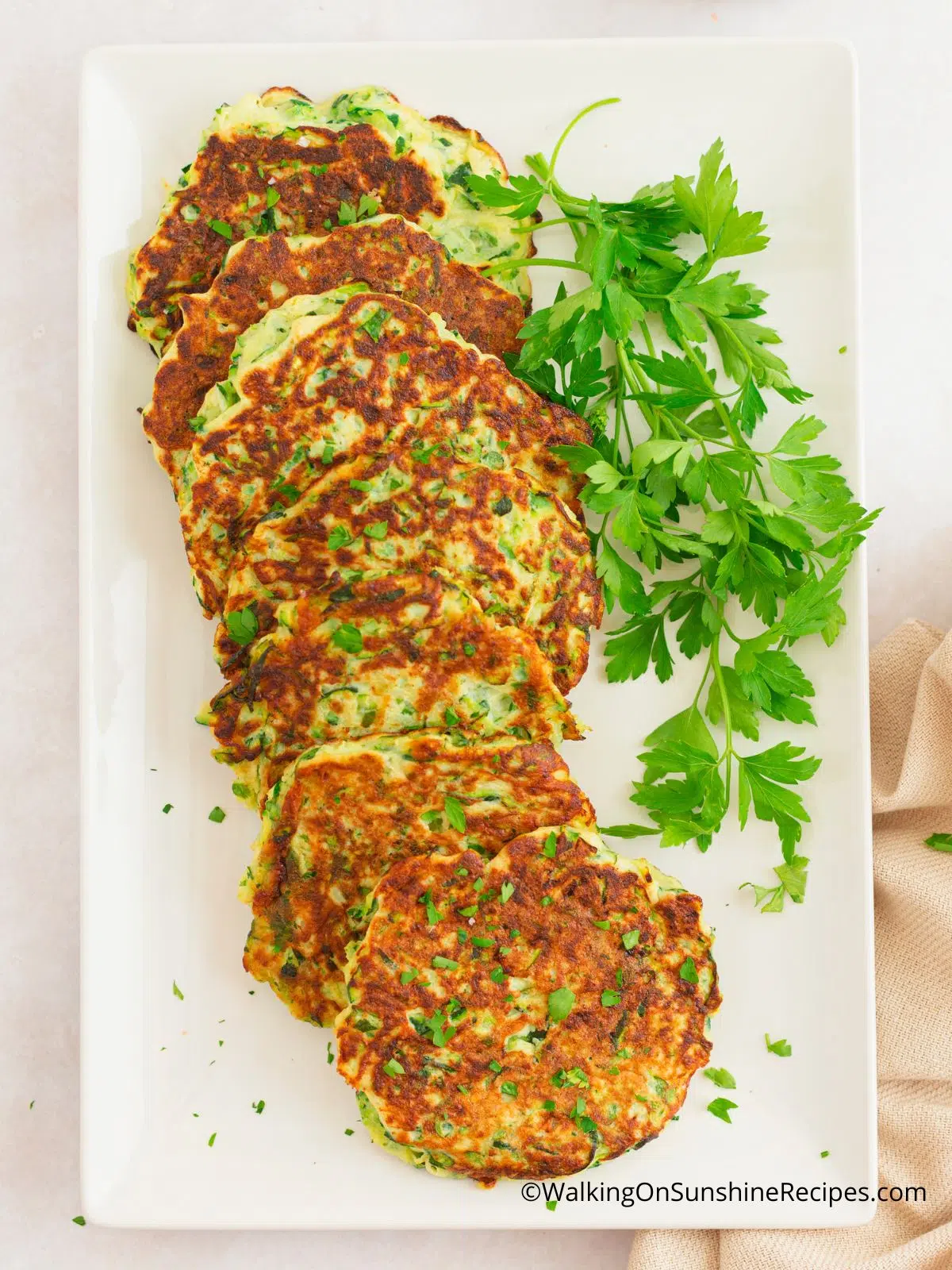 Zucchini fritters on white plate with fresh parsley as garnish.