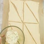 Pillsbury crescent rolls on parchment paper with garlic butter in bowl.