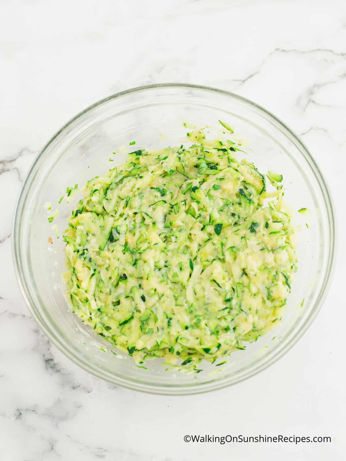 grated zucchini and ingredients in glass bowl.
