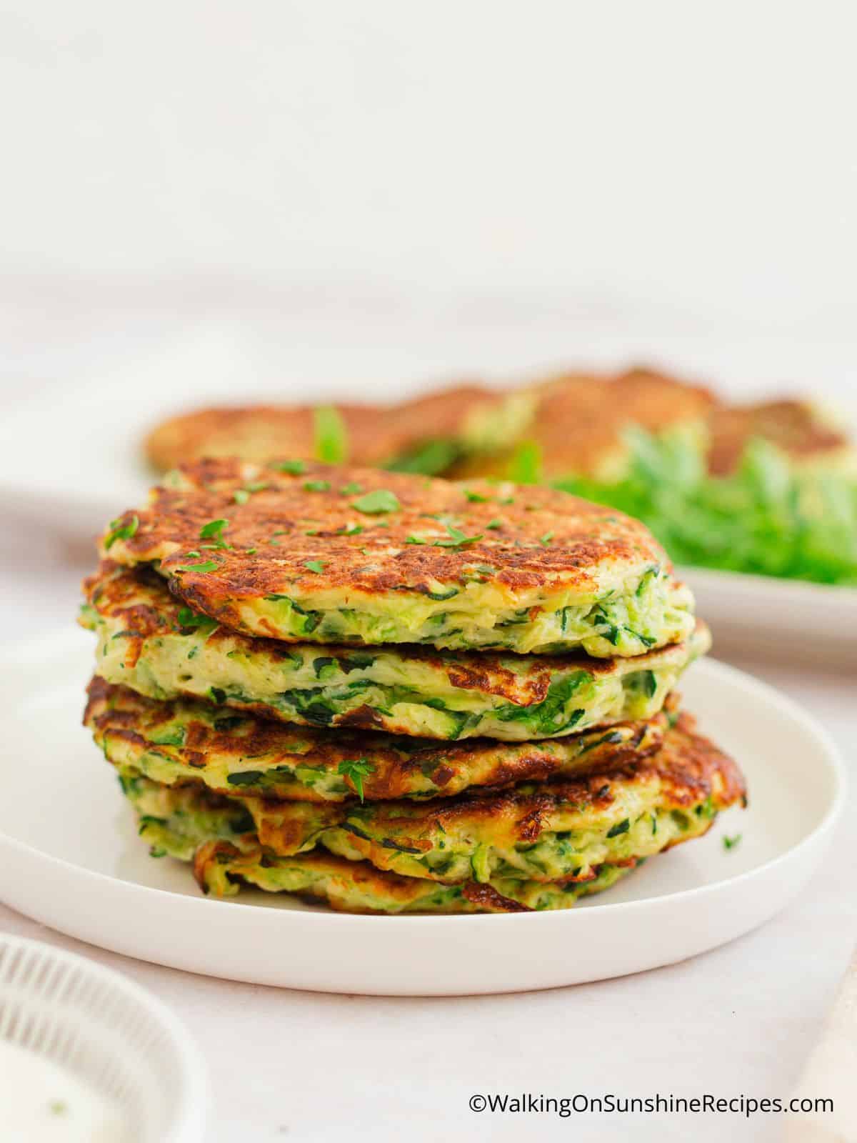 zucchini fritters ready to serve. Stacked on a white plate.