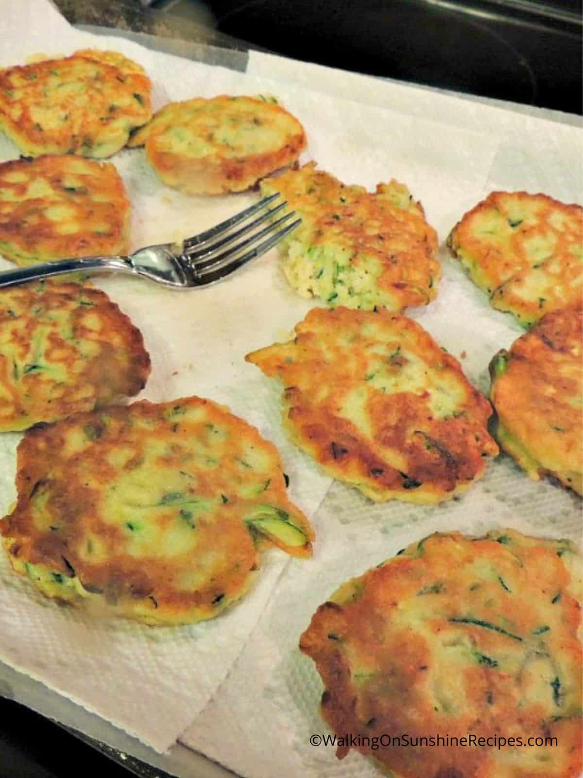 Zucchini fritters on paper towel after frying with fork.