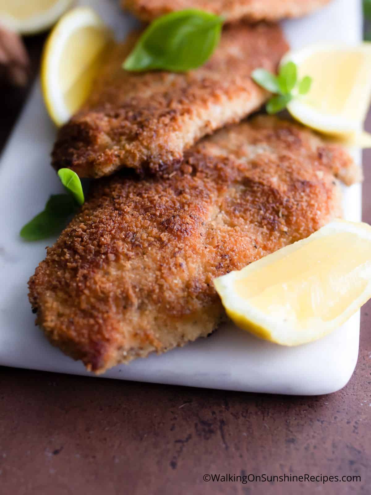 closeup of Italian chicken cutlet with lemon wedge.