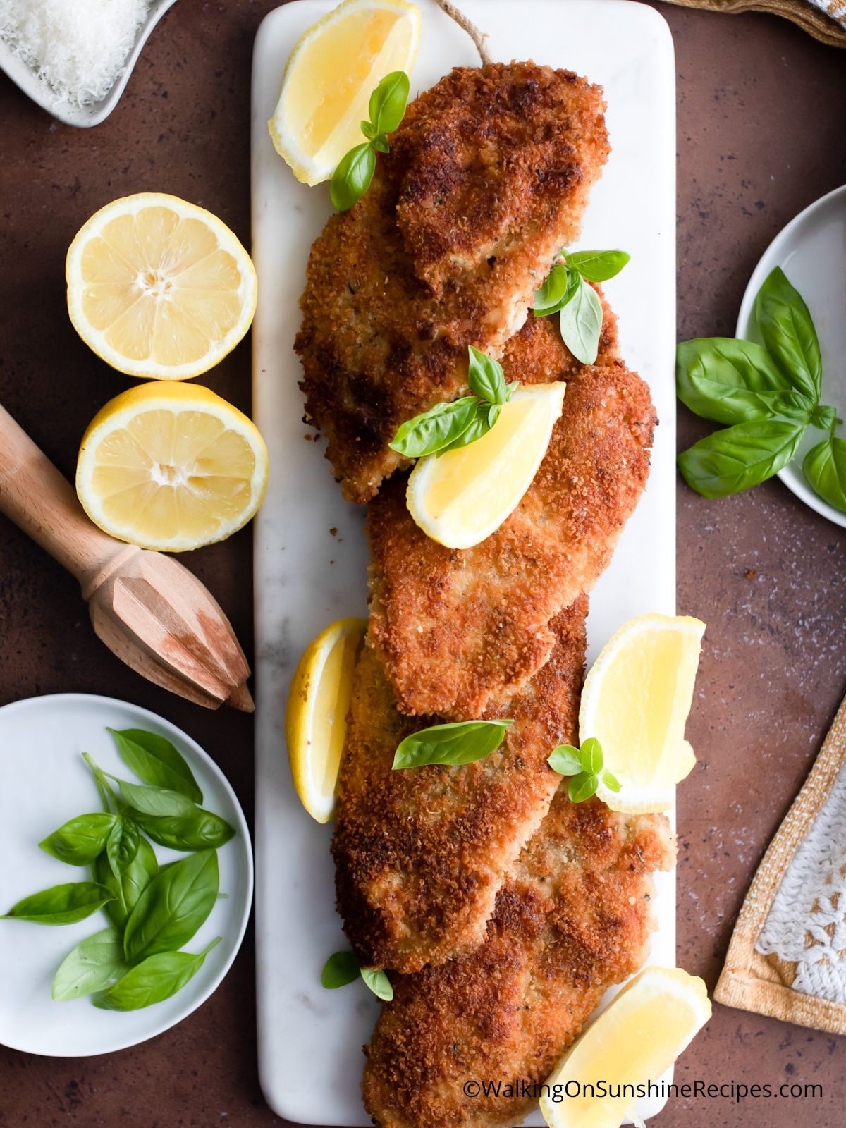 Breaded fried Italian chicken cutlets on white plate with lemons.