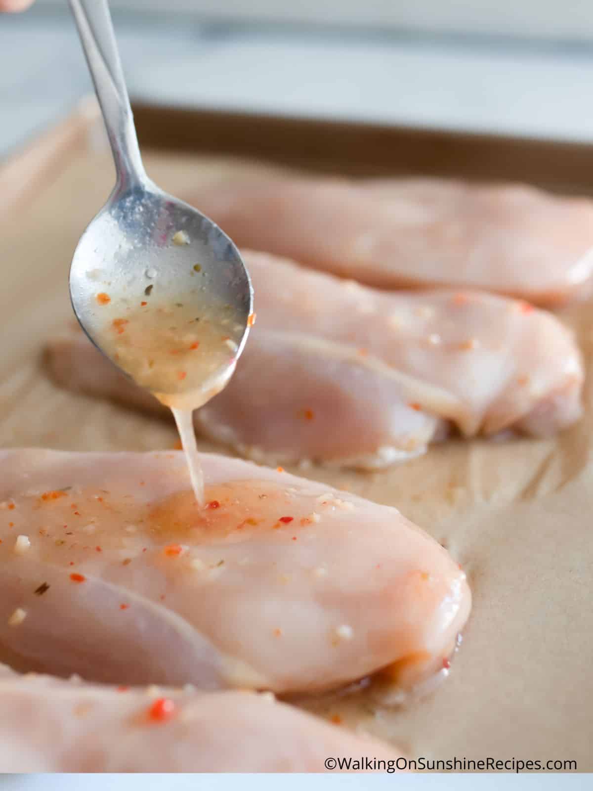 spoon Italian dressing marinade on top of raw chicken cutlets.