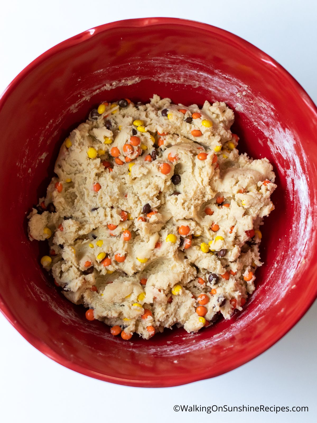 Cookie batter with Reese's pieces combined in red mixing bowl.