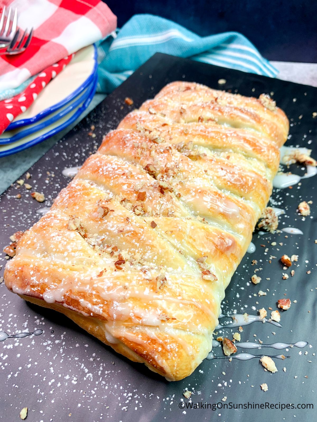 Chocolate puff pastry on serving tray with glaze and chopped pecans.