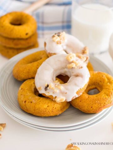 Homemade pumpkin donuts on plate with powdered sugar glaze and chopped walnuts.