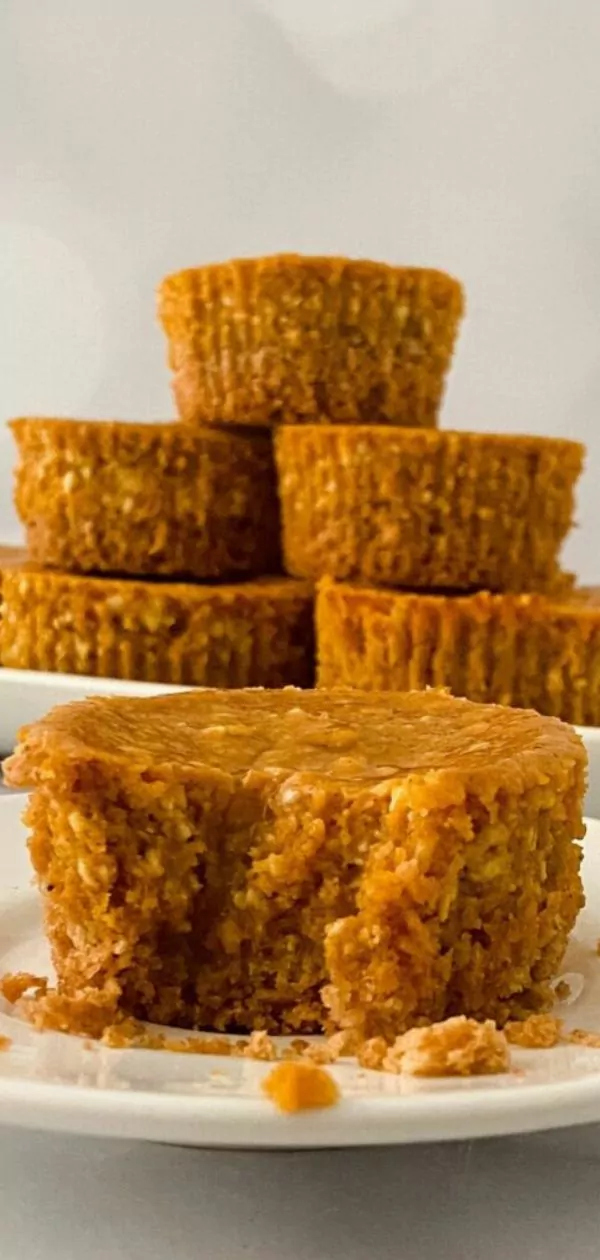 a pumpkin cheesecake cupcake with a bite taken out in the foreground. In the background is the rest of the pumpkin cheesecakes stacked up on a platter.