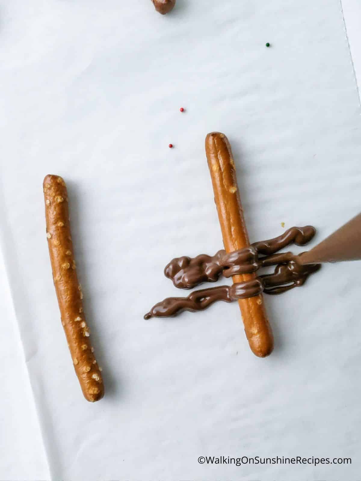 Add melted chocolate to the back of a pretzel stick.