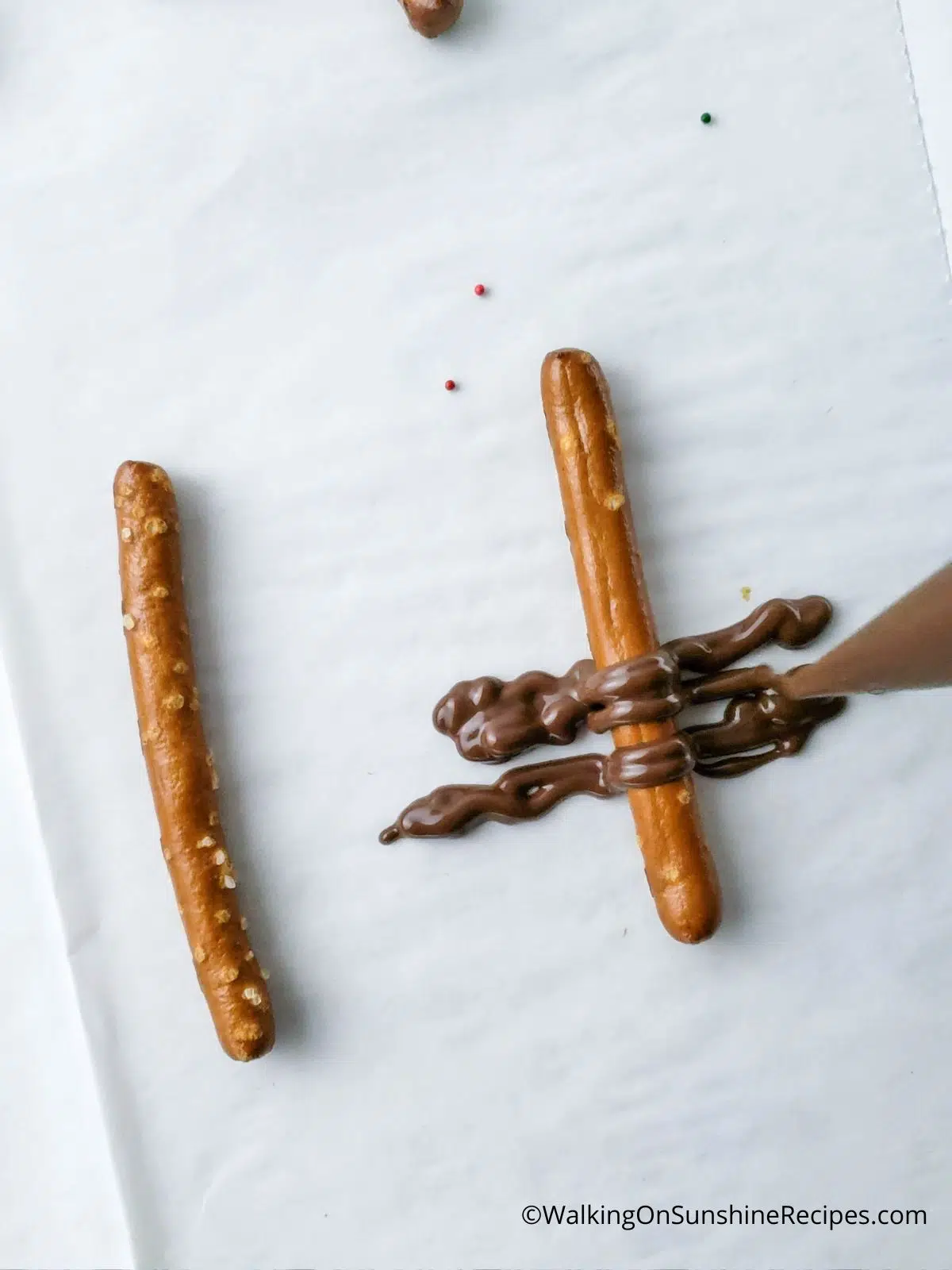 Add melted chocolate to the back of a pretzel stick.