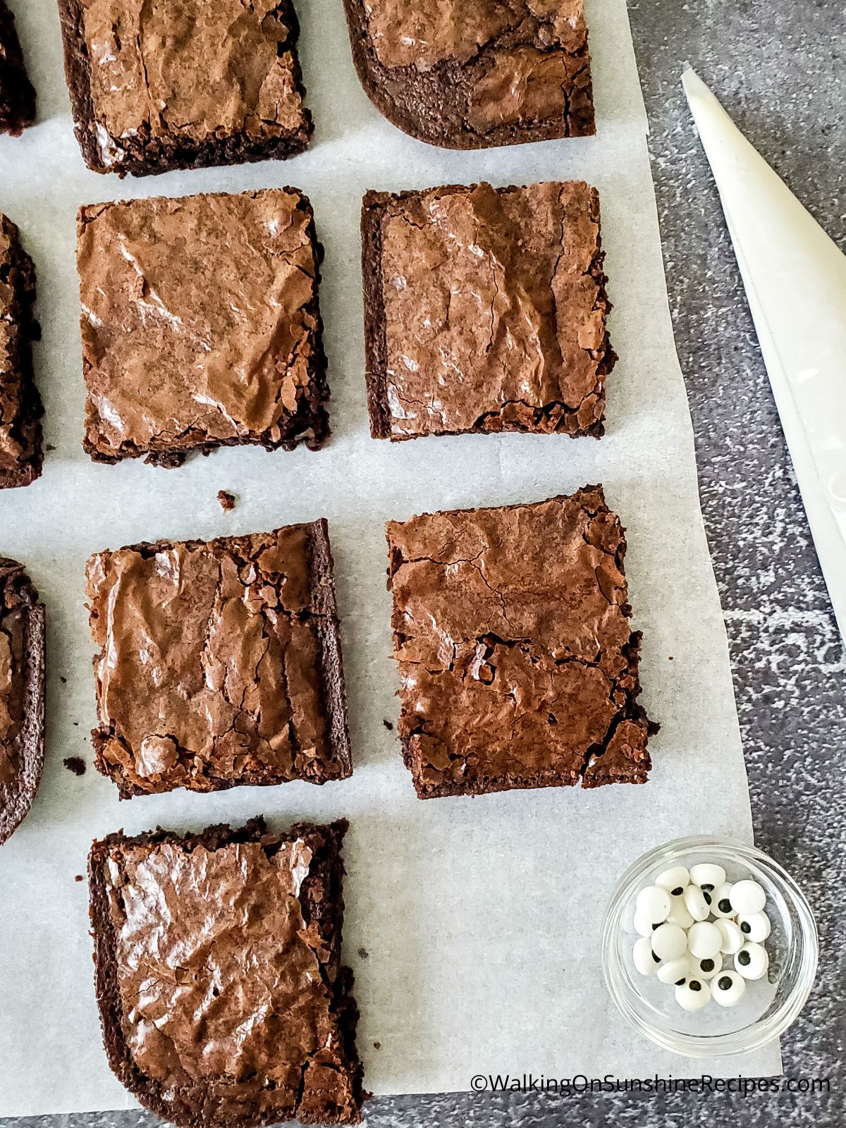 Cut brownies on parchment paper with vanilla frosting in piping bag.