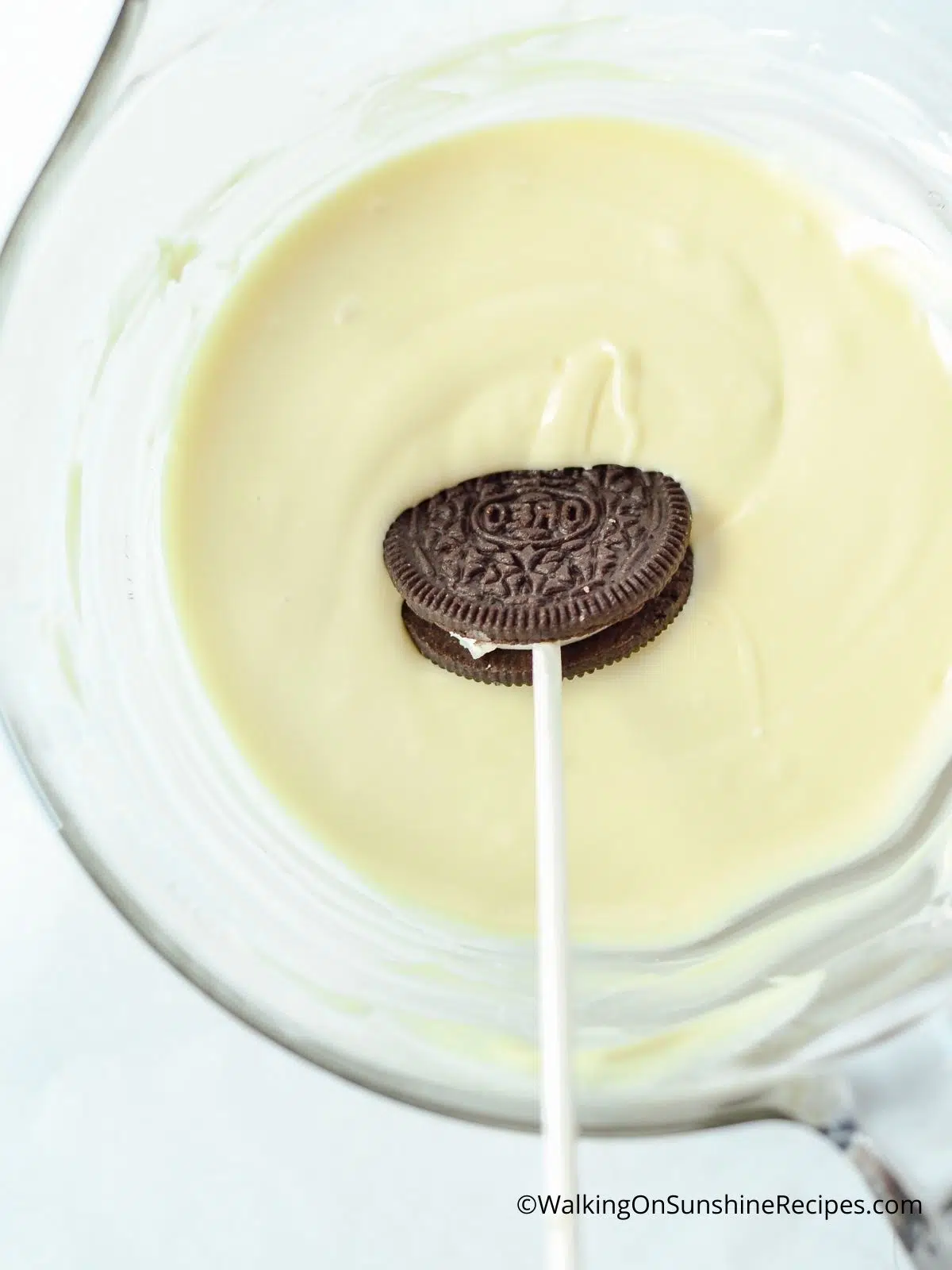 Dipping Oreo cookie on a stick in melted white chocolate.