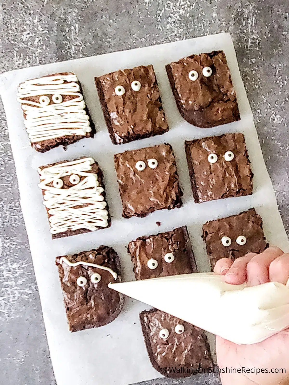 Decorate brownies with vanilla frosting to resemble mummies.
