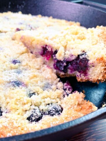 Homemade blueberry coffee cake sliced and being served from skillet pan.