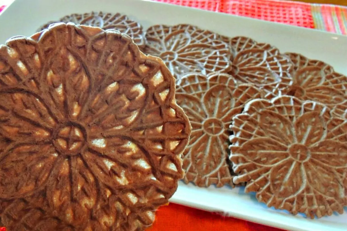 close up of a chocolate pizelle cookie with the platter of cookies in the background