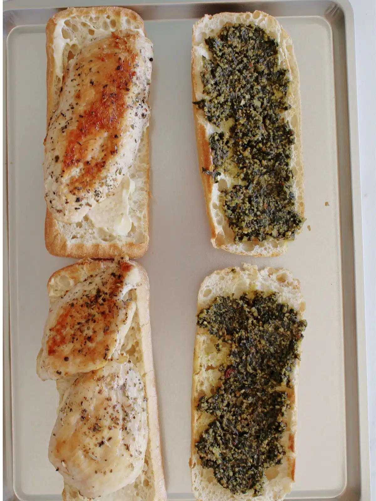 Sandwich being assembled on a sheet pan with pesto and chicken