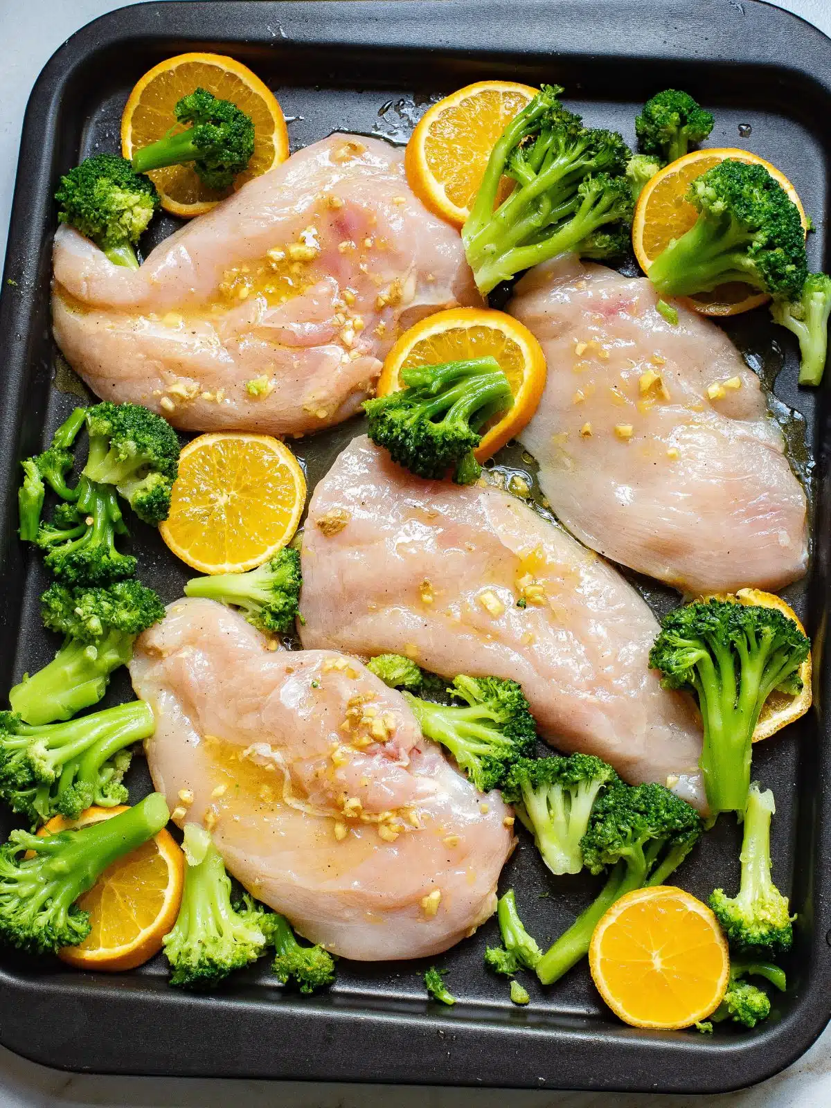 chicken cutlets, broccoli, and orange slices on a sheet pan before baking