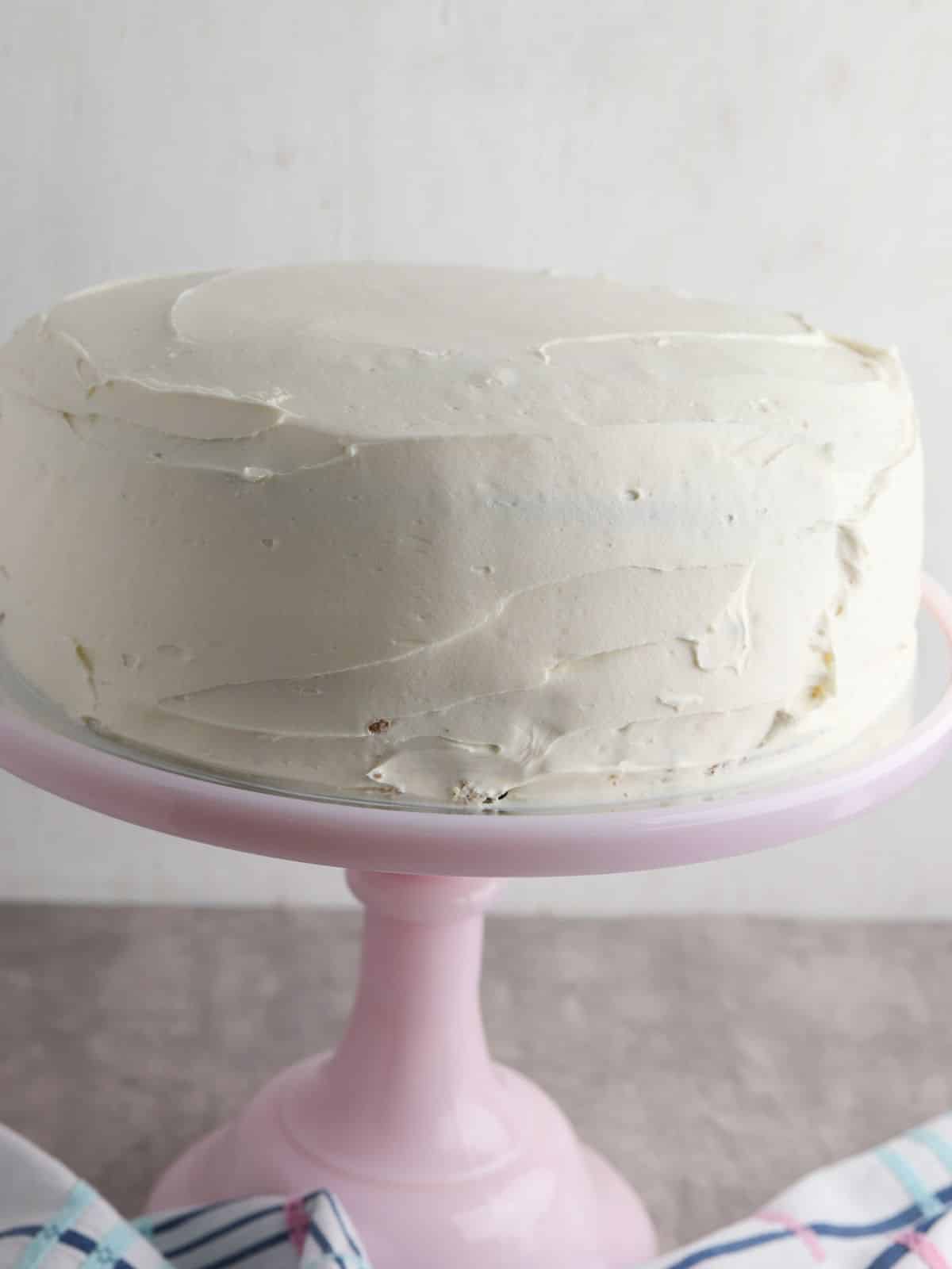 cream cheese frosted cake on pink cake stand.