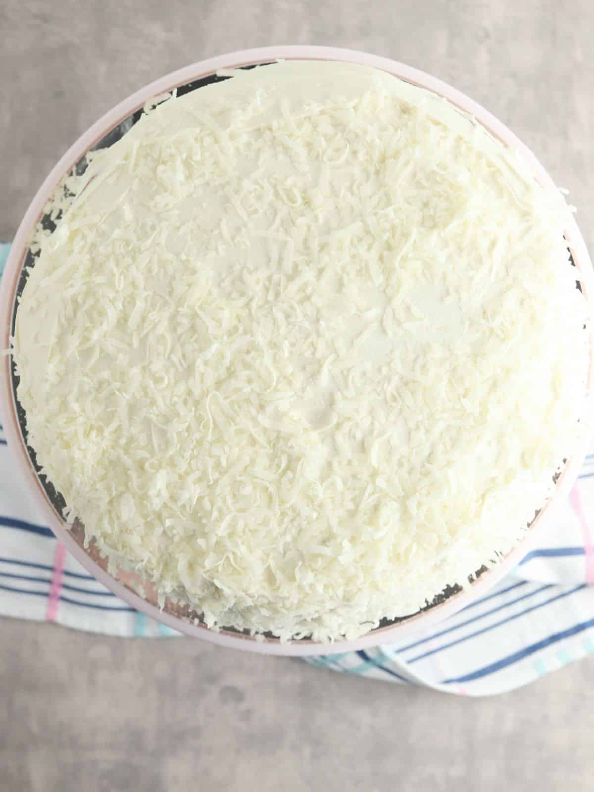top of round cake on cake stand with frosting and shredded coconut.