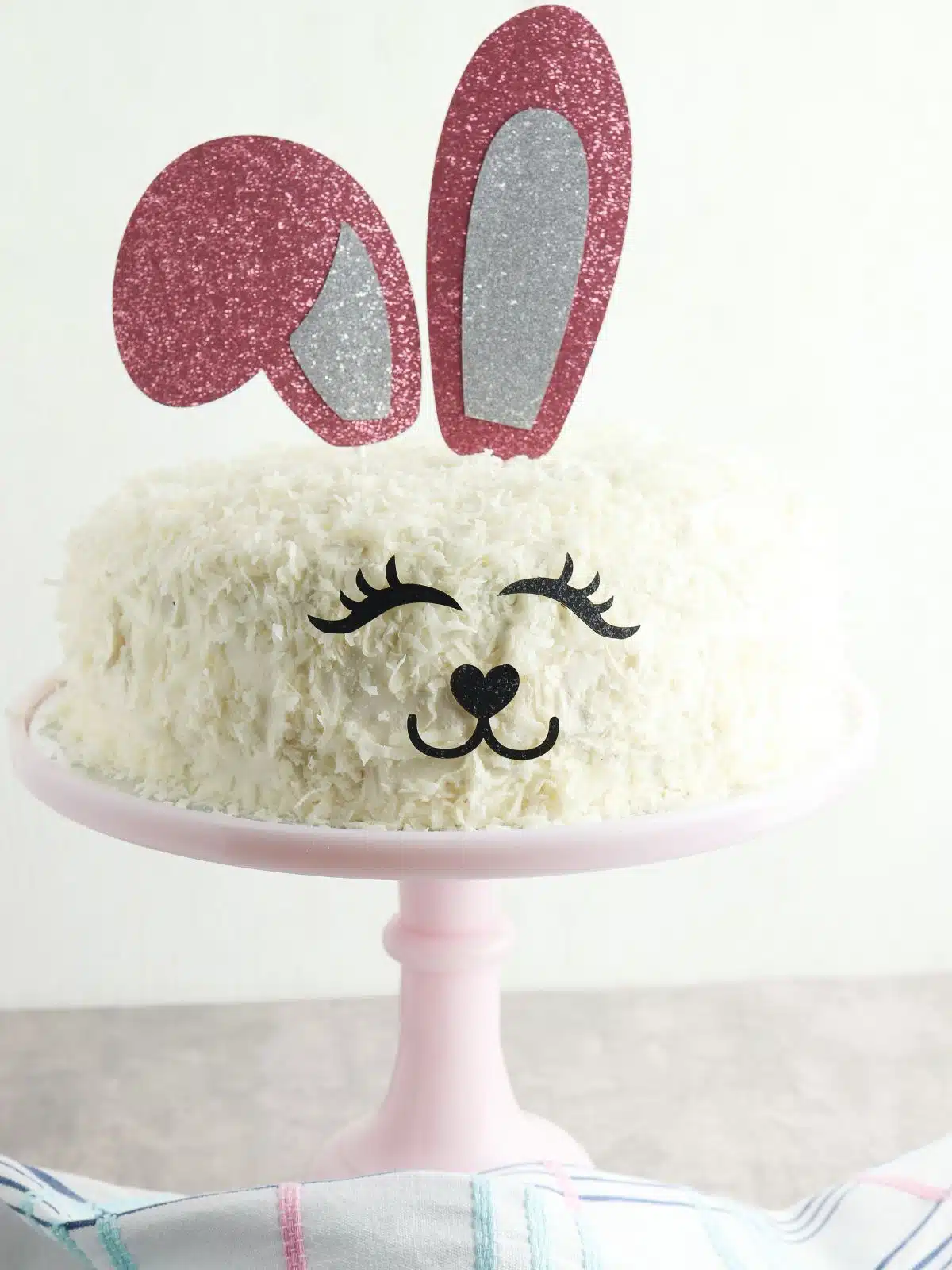 round cake with bunny ears, eyes and nose on pink cake stand.