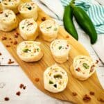 Cream cheese pinwheels sliced on cutting board with bacon pieces.